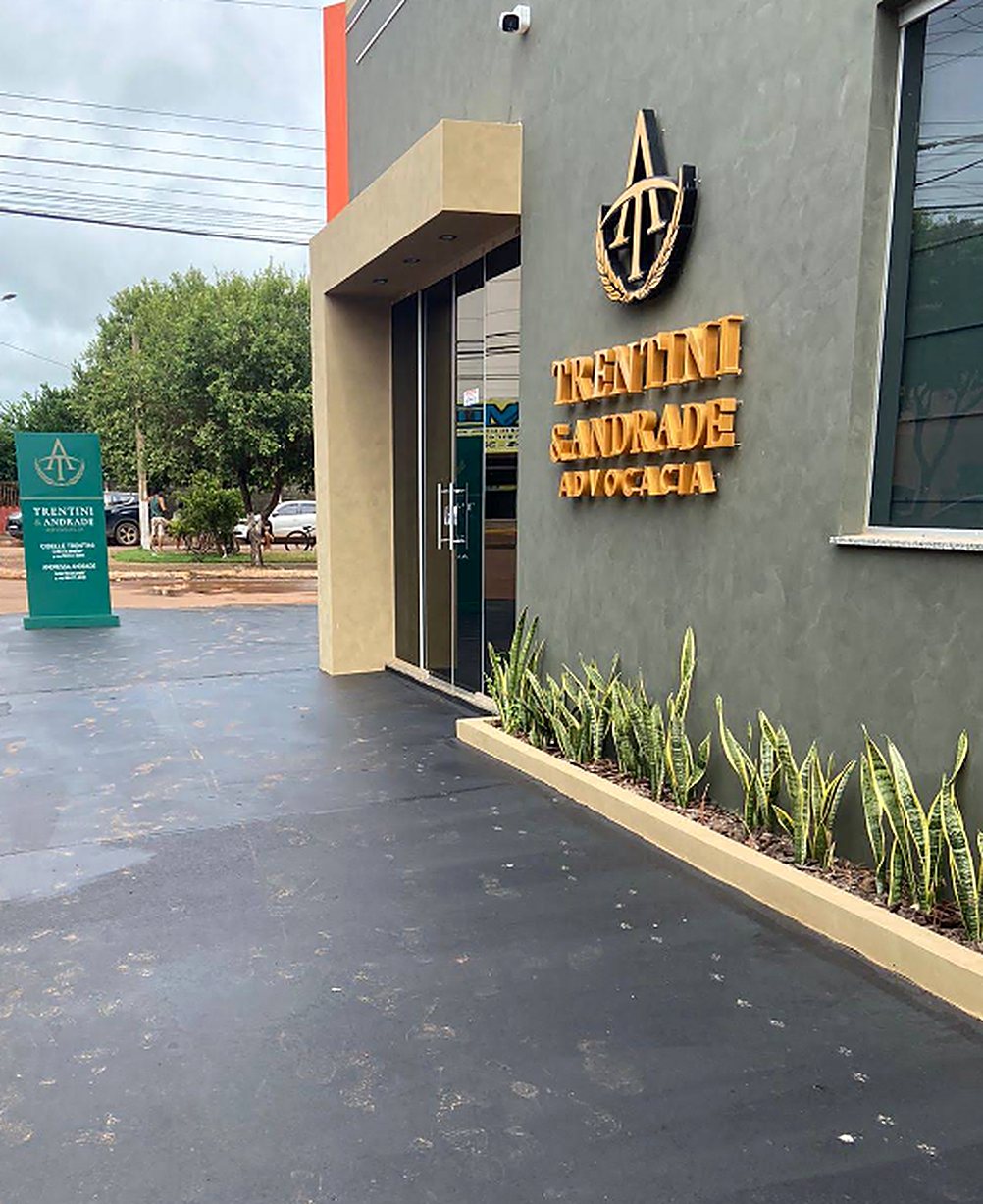 Entrada do escritório Trentini e Andrade em Confresa, Mato Grosso, com a logo dourada na parede verde e o totem com o nome das sócias
